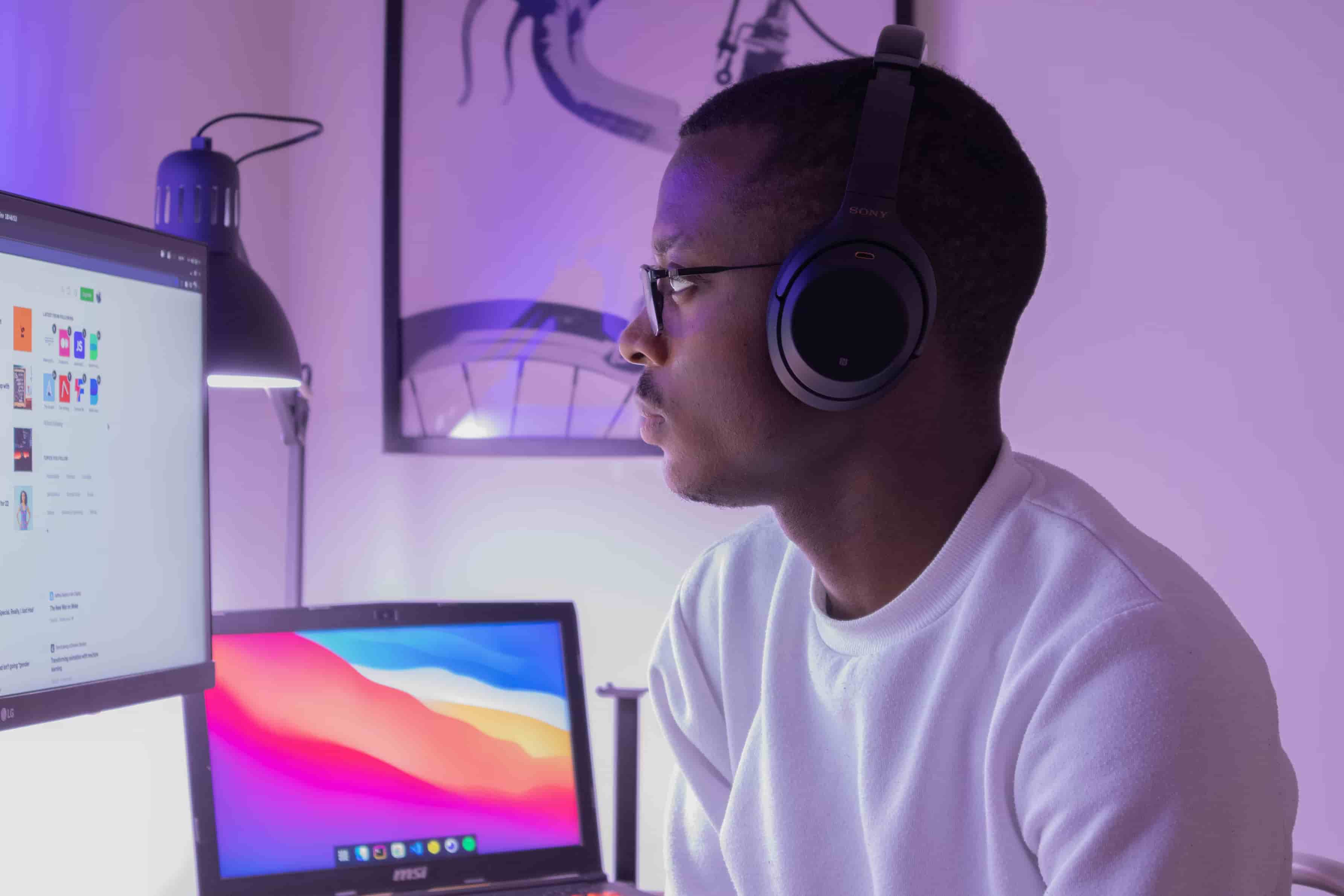Man wearing headphones, focused on a screen with a glowing laptop in the background.
