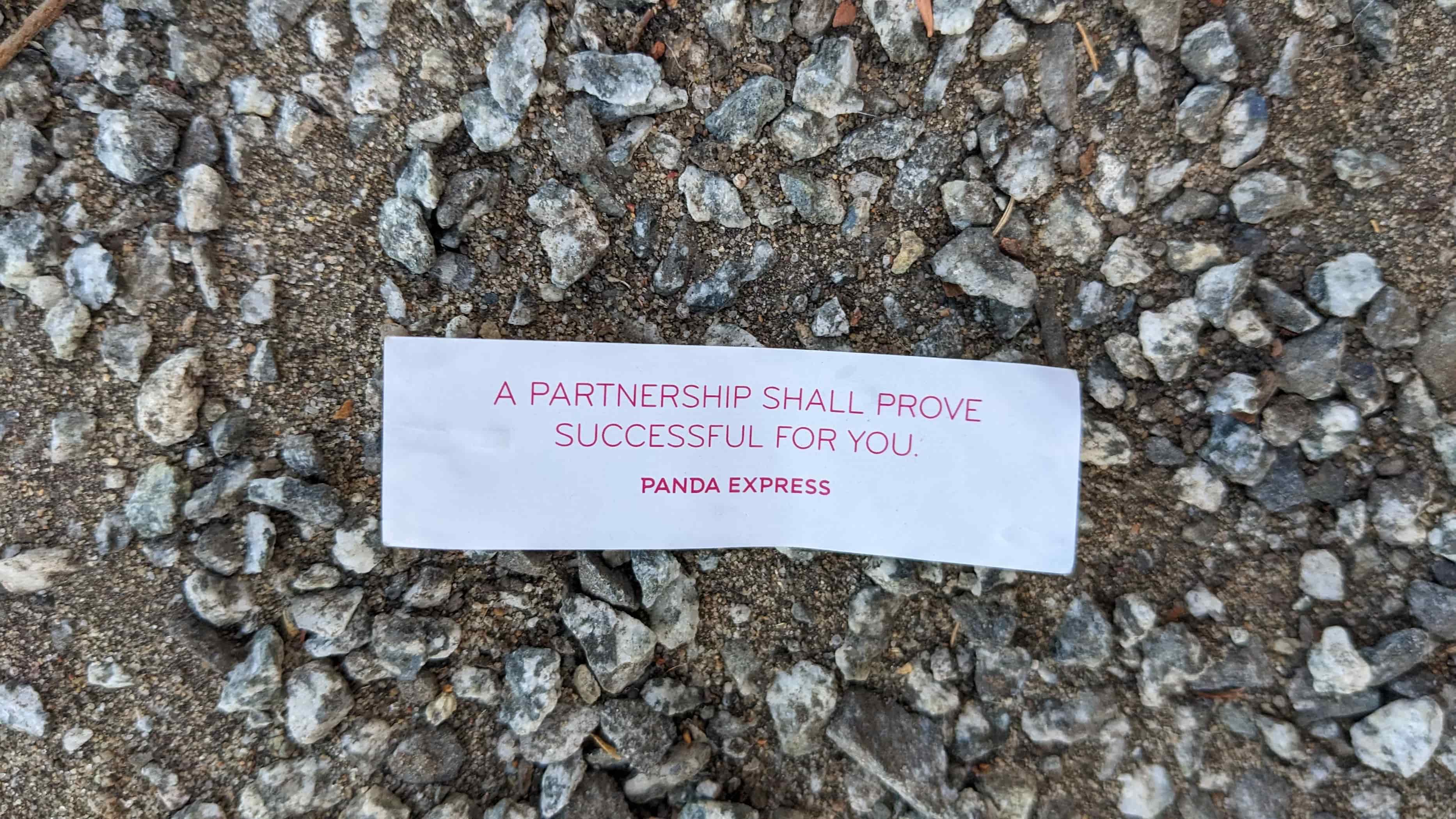 A paper fortune lying on gravel reads: “A partnership shall prove successful for you. — Panda Express.”