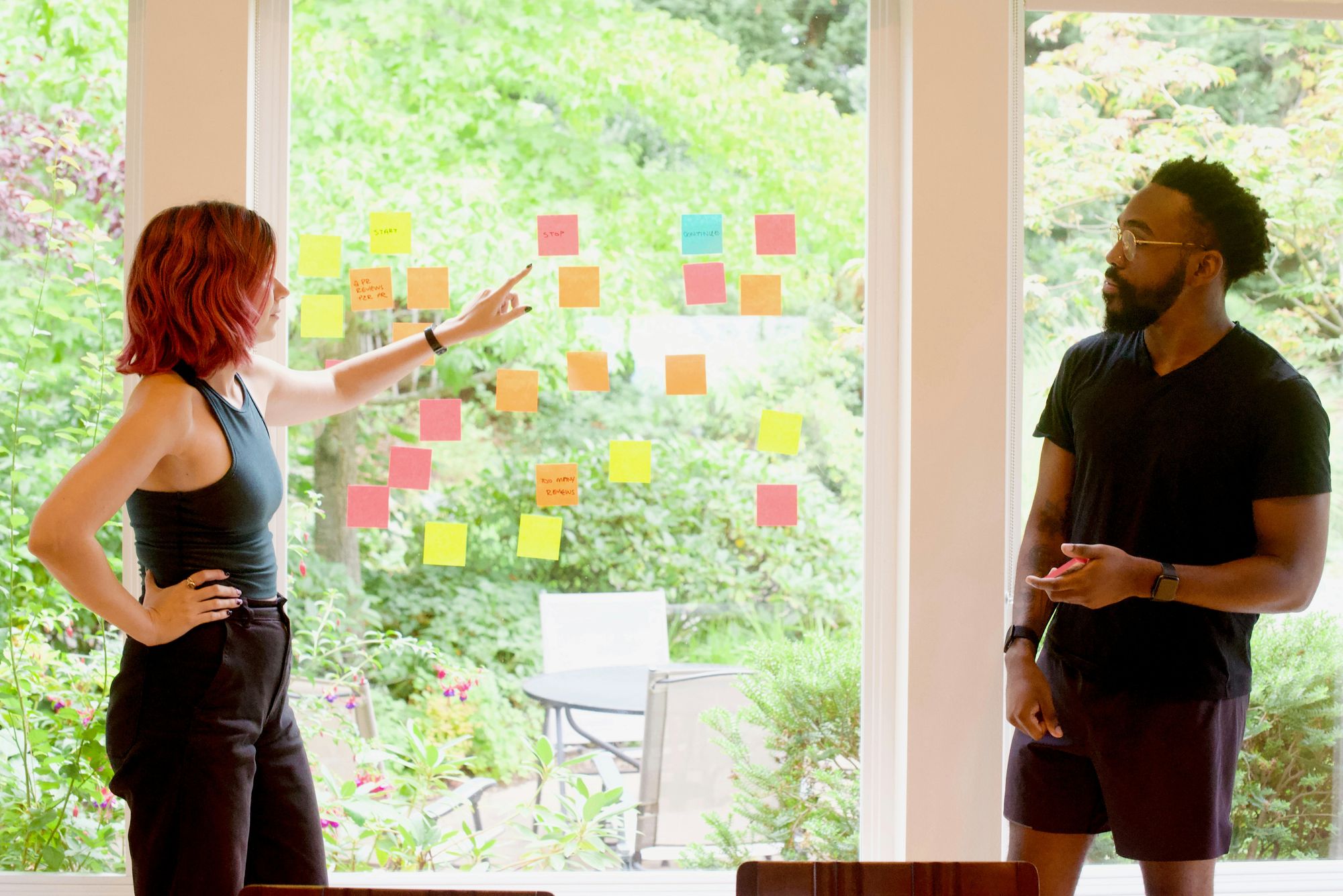 Two people arranging colorful sticky notes on a large glass window 