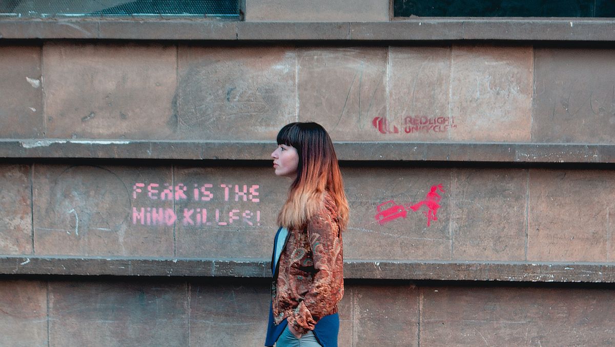                                                   A woman next to a wall with the writing "Fear is the mindkiller".